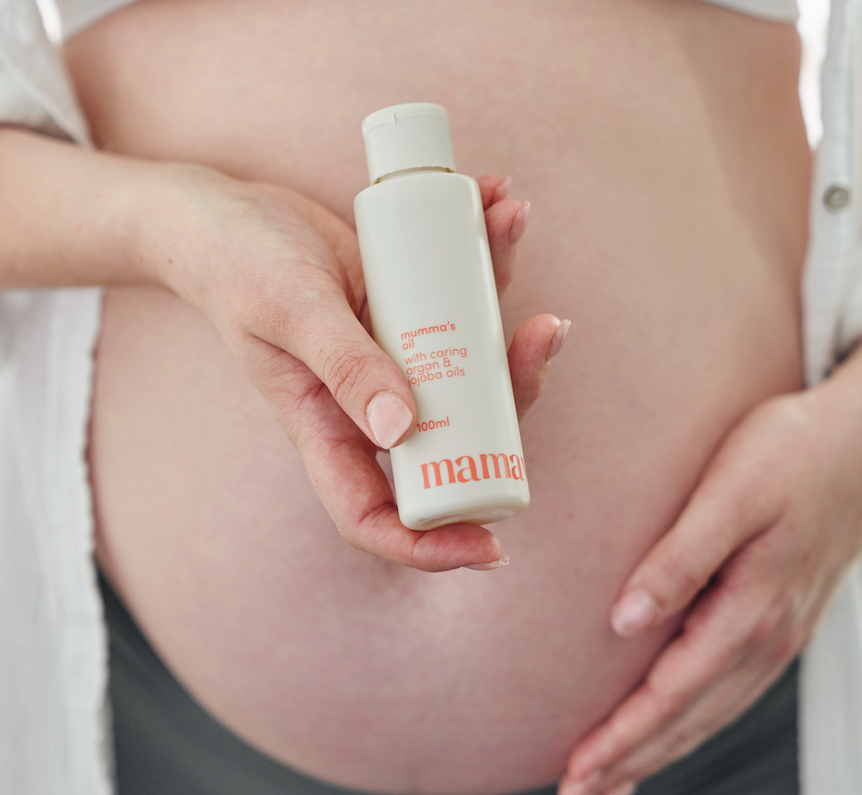 pregnant woman holding mumma's oil in front of her belly
