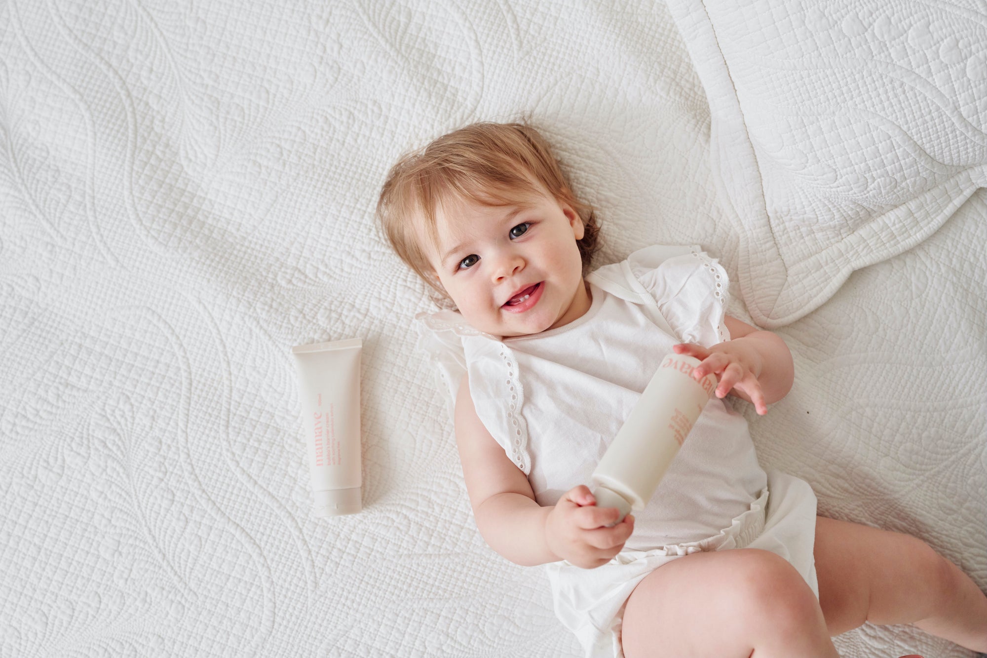 baby laying on bed looking up at camera with products in her hand